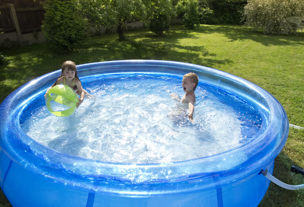 Dwoje dzieci bawiących się wodą w nadmuchiwanym basenie w ogrodzie.