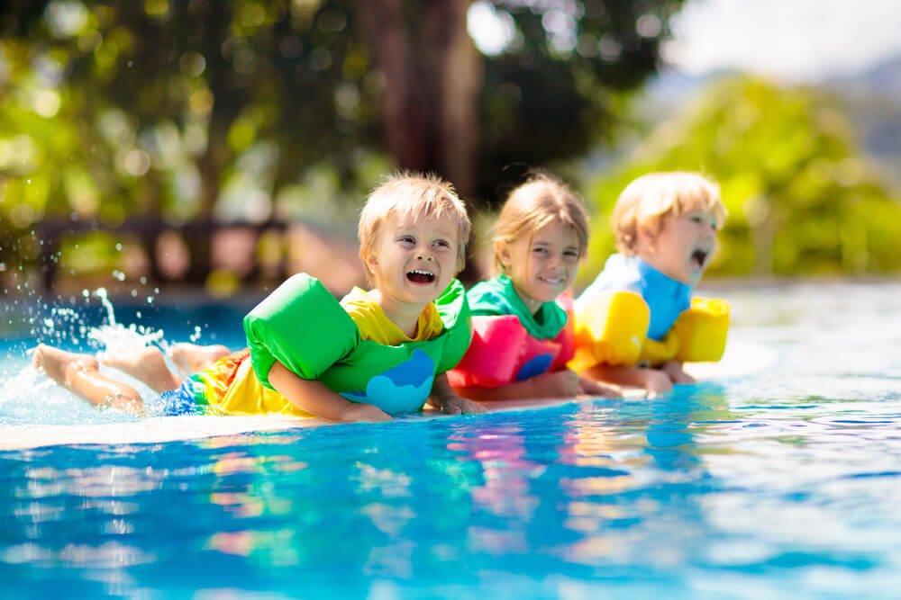Grupa dzieci w wieku do 6 lat bawiących się w wodzie w kolorowych kamizelkach pływackich